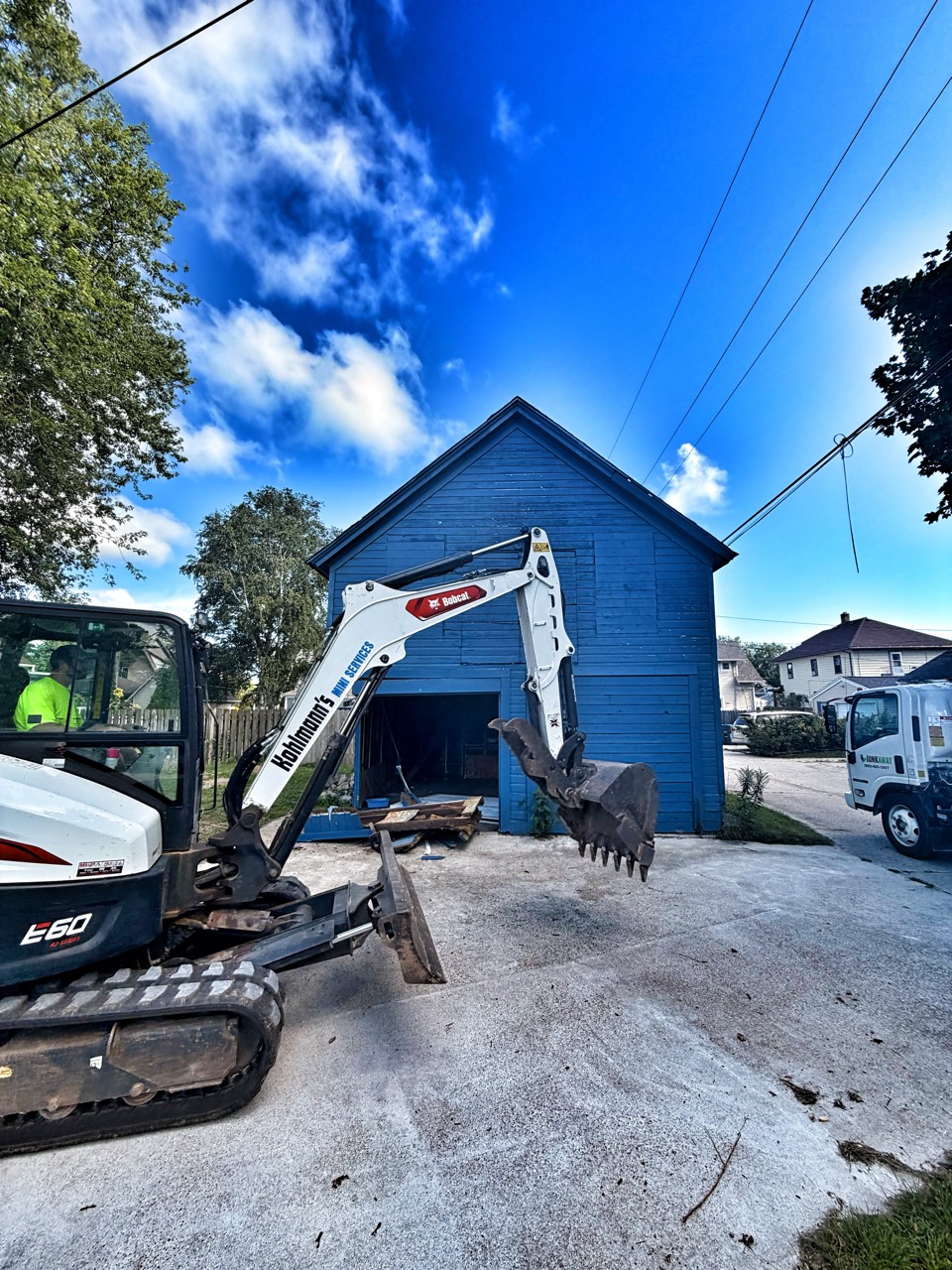 Excavation equipment beside a blue garage with demolition underway